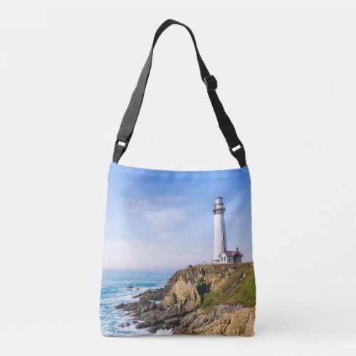Lighthouse on hill blue sky white house ocean crossbody bag