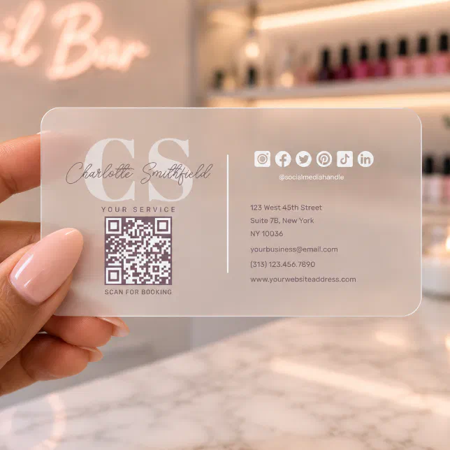 A frosted business card with a QR code is held in a person's hand. A nail bar can be seen in the background. 