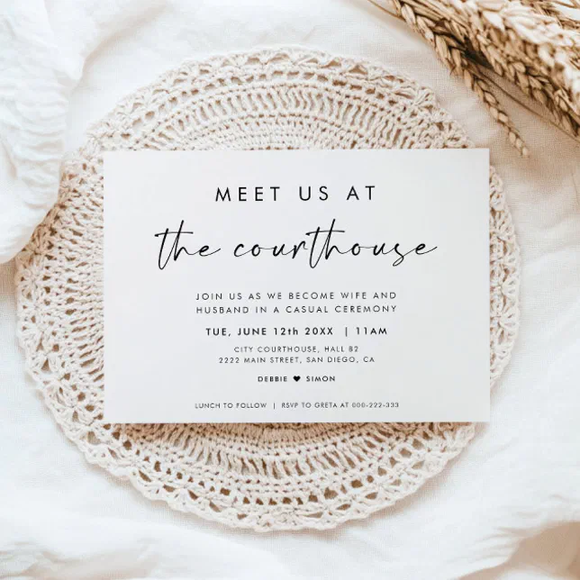 A white invitation is on top of a laced doily beside some dried florals.