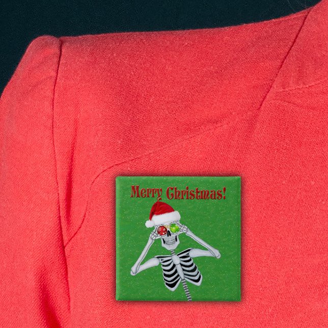 Merry Christmas Happy Skeleton Santa Hat Green Button (Happy Christmas skeleton holding ornaments in Santa Hat on green with gold flecks pin back button.)