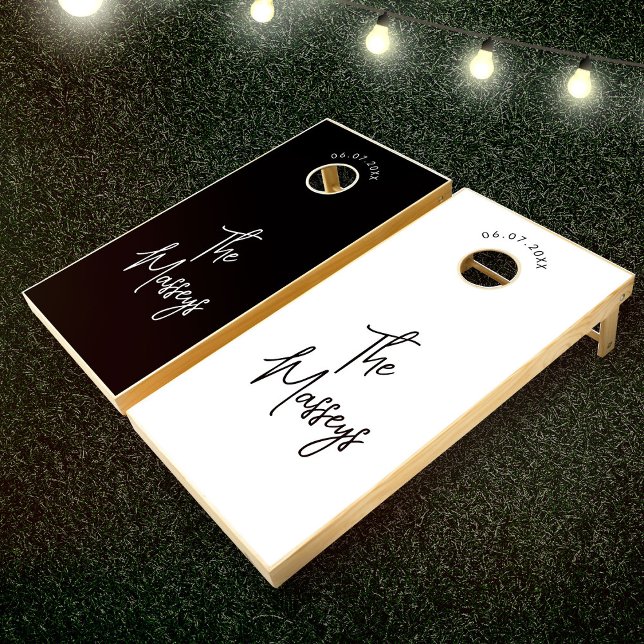 Minimalist Wedding Guestbook Black and White Cornhole Set (Two cornhole boards on grass with string lights above. One board is black, the other white with name)