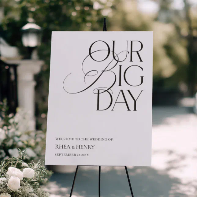 A modern welcome sign to a couple's wedding day placed at the entrance to their venue, with lush greenery in the background.