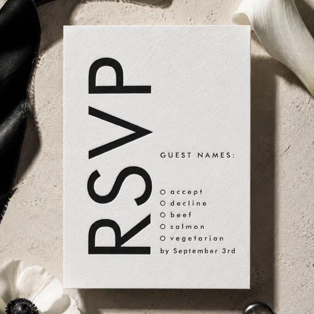 A bold monogram letterpress RSVP card surrounded by some white petals.