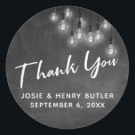 Modern Chalkboard & Edison Lights Thank You Classic Round Sticker<br><div class="desc">In this pretty wedding-themed design I've used an elegant, modern calligraphy font to create a white graphic typography overlay reading Thank You. The background was covered with an image depicting a textured chalkboard. Overlaying that is a cluster of round white vintage Edison lights. Fill in the template blanks with your...</div>
