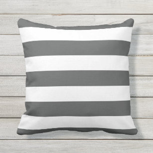 A charcoal gray striped lumbar pillow sits atop a wood and wicker accent  chair positioned at the corner of a white and gray…