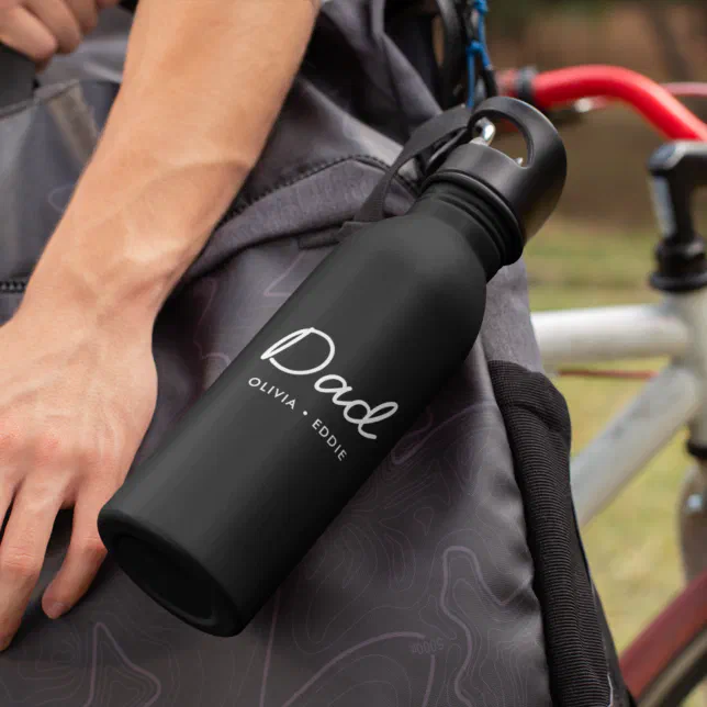 A black water bottle with the word "Dad" is featured clipped onto a bag. In the background is the top half of a bicycle.