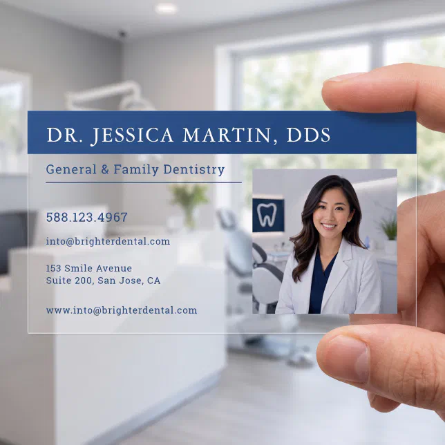 A clear business card with a photo of a dentist is held in a person's hand. The dentist's office can be seen in the background. 
