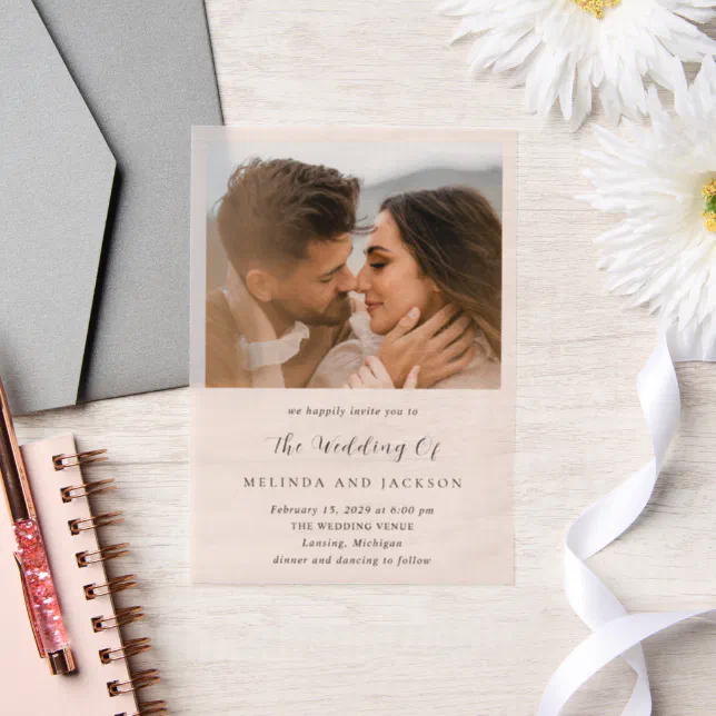A wedding invitation with a vellum overlay depicting a couple about to kiss. A notebook, envelope, and some flowers are in the background. 