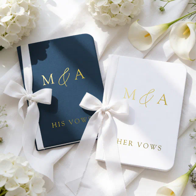 A pair of blue and white vow books rest on a white sheet surrounded by white flowers. 