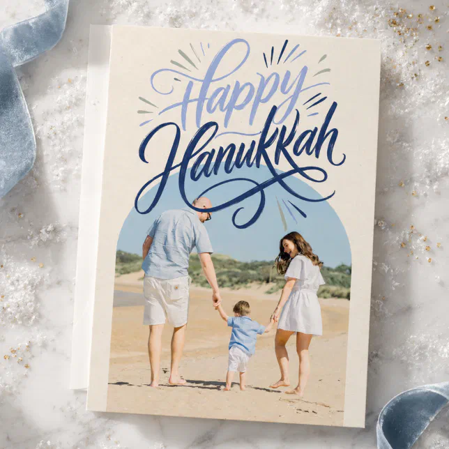 A blue and cream Hanukkah hard with blue ribbon and white snow-like decorations in the background.