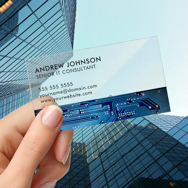 A person holds a clear business card in their hand that has a blue color scheme and a circuitry-theme design. Skyscrapers can be seen in the background.