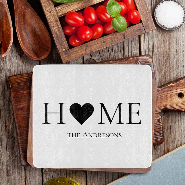 A white cutting board with a heart motif is set next to a bowl of salt, tomatoes and basil. There are also some wooden kitchen utensils in the frame.