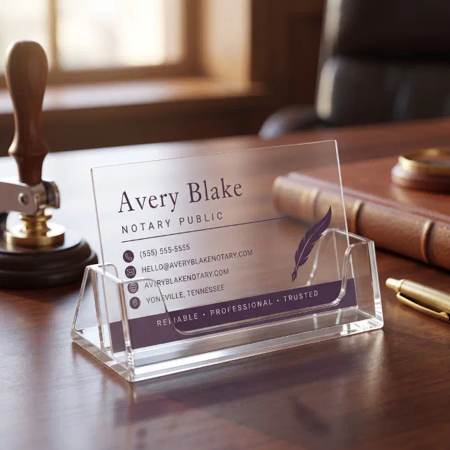 A purple-themed clear business card with a quill motif sits in a business card holder. 