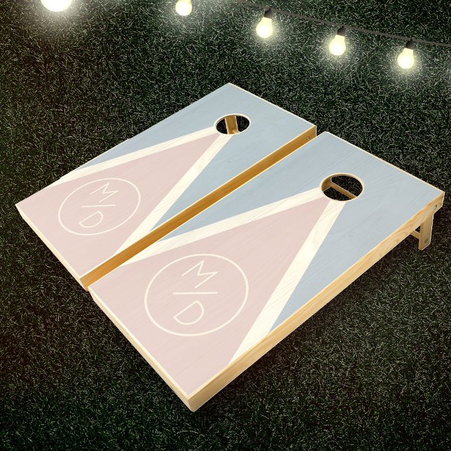 Modern Romantic Blush Blue Monogram Wedding Cornhole Set (Two pastel-colored cornhole boards with triangular designs and the letters "M/D" on each on grass)