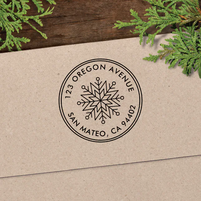 A stamp with a black snowflake motif is shown printed on a brown envelope with some greenery next to it.