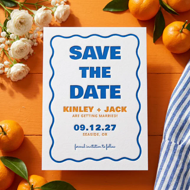 A letterpress Save the Date can be seen atop an orange table surrounded by oranges and flowers.