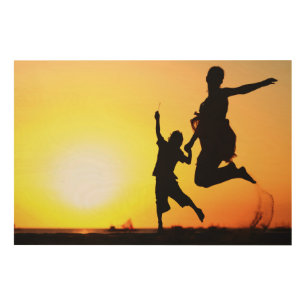 Mother and son silhouettes jumping on beach at sun wood wall art