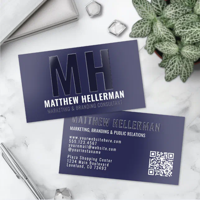 A navy blue spot UV business card featuring a QR code is lying on a marble surface.