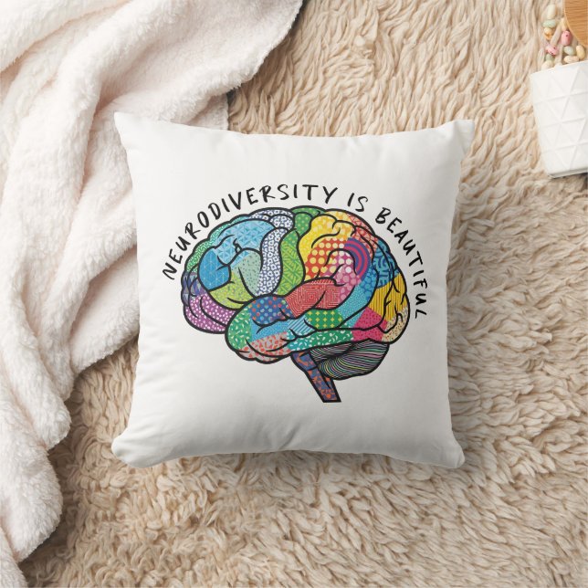 A white pillow with a colorful brain print is shown laying on a cream rug next to a white blanket.