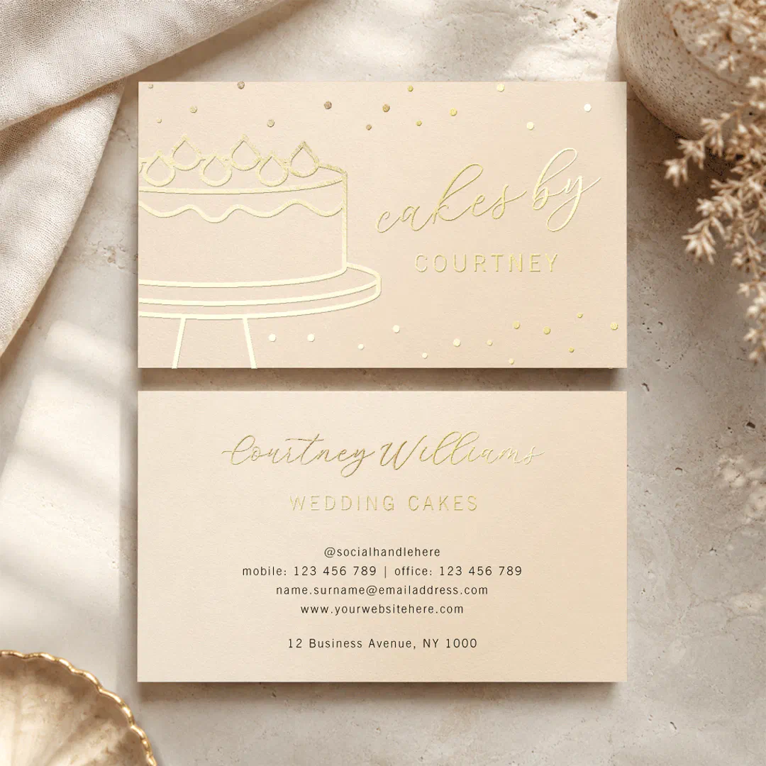 A double-sided business card with gold foil text and normal black font at the end. There's a stick image of a cake on a cake holder. Neutral tones fill the background.