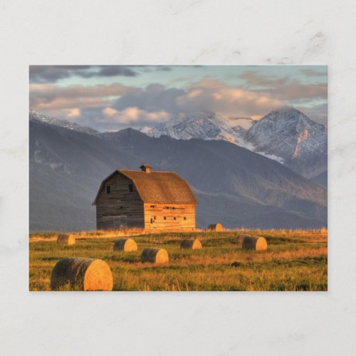 Old barn framed by hay bales and dramatic postcard