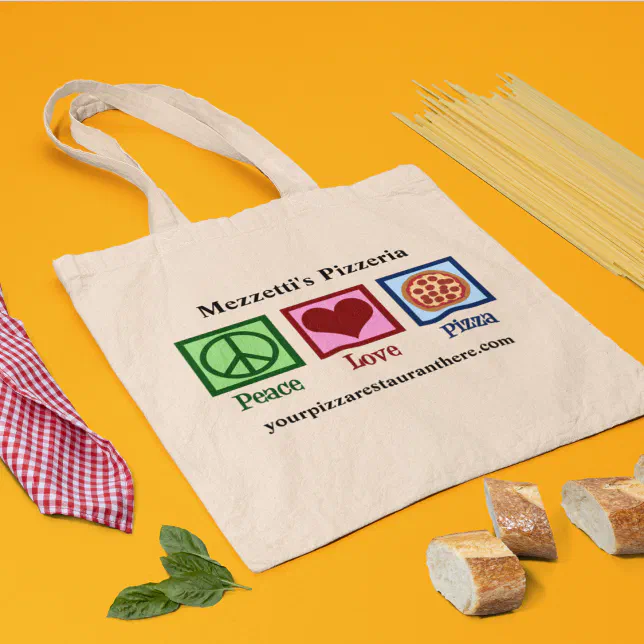 A tote bag rests on a yellow-orange background with spaghetti, bread, basil, and a napkin pictured around it.