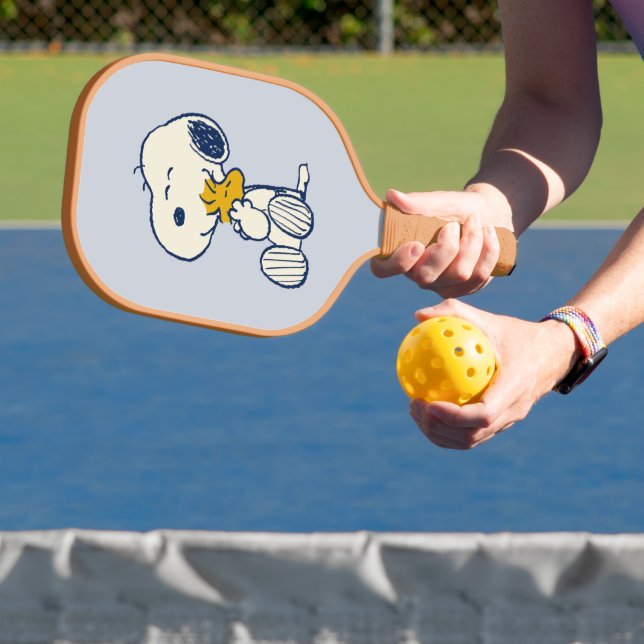 A person plays pickleball in a court with a Snoopy design on their paddle.