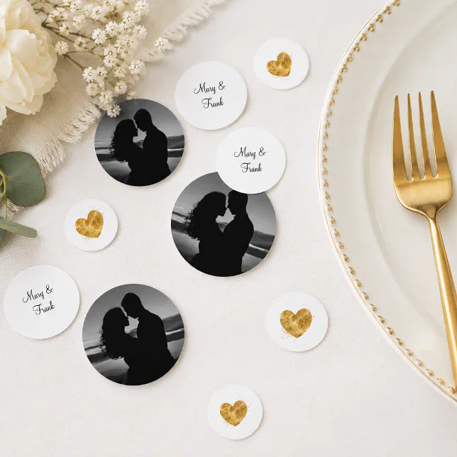 Custom wedding table confetti scattered on a table. In the frame there is some flowers, a napkin, a plate and a gold fork.