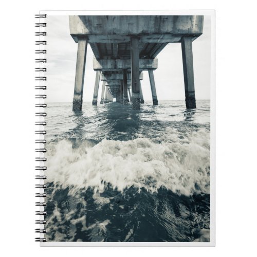 Pier with waves crashing on beach shore notebook