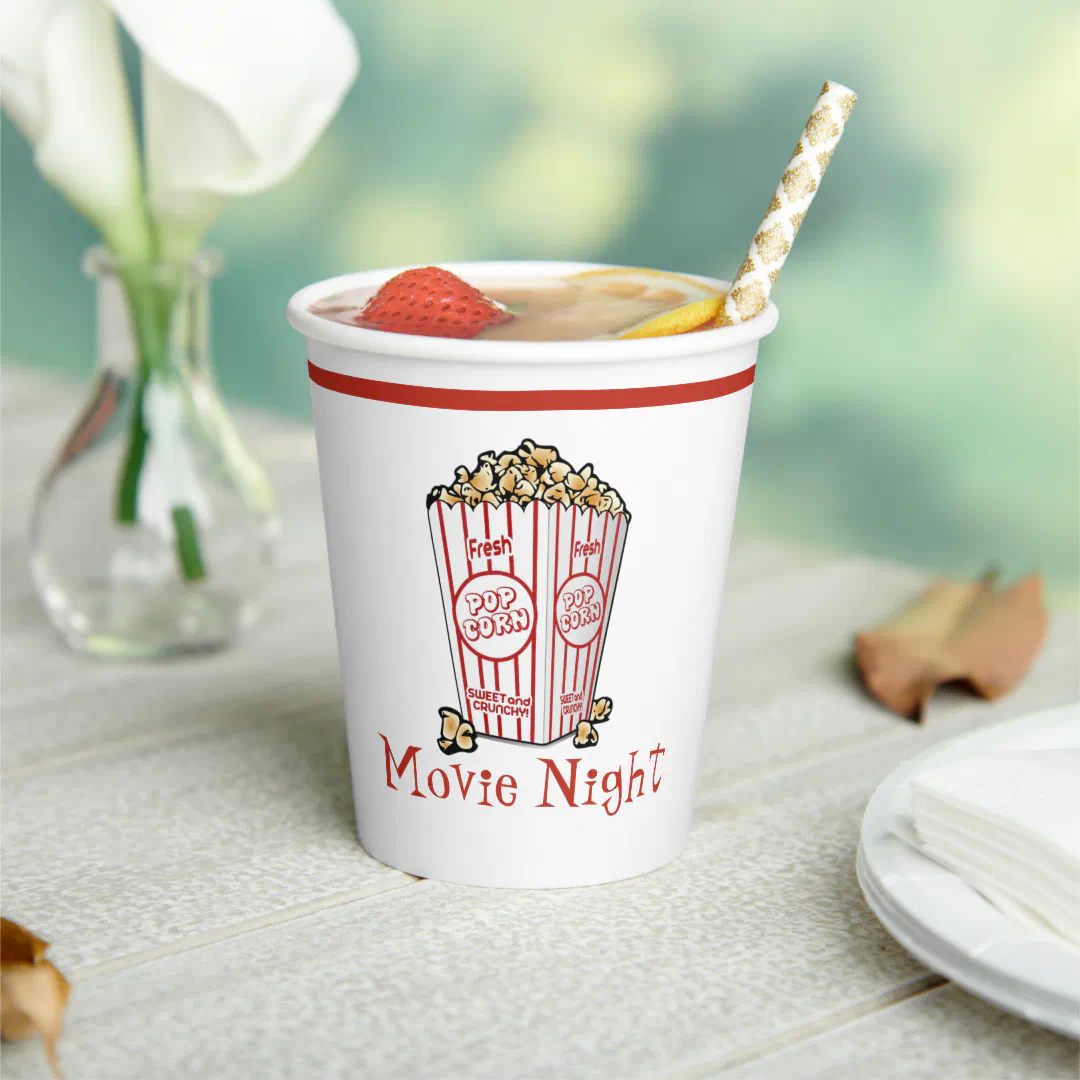 White paper cup with a retro popcorn bucket illustration and text, filled with fruit punch and a gold straw.