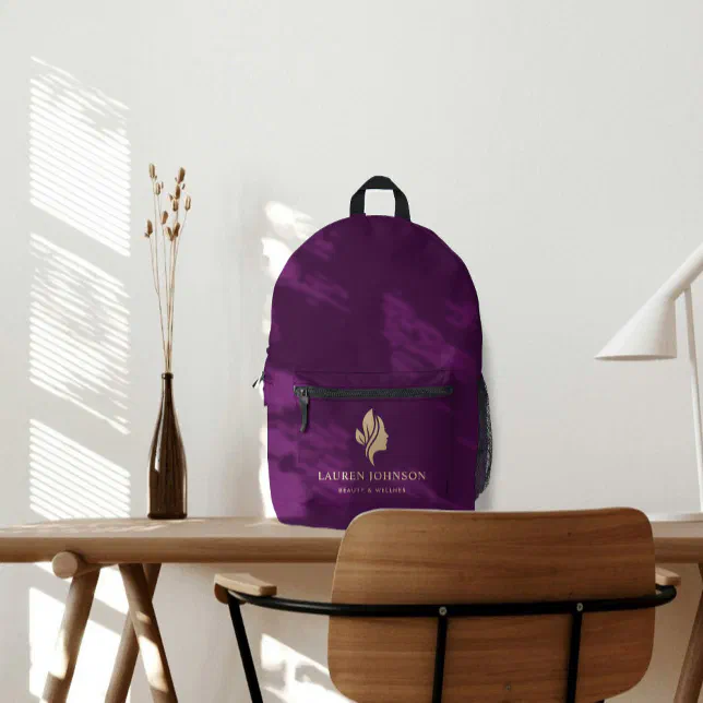 A purple backpack sits on a desk, a chair pictured in front, a white lamp to the right, and a glass bottle with dried flowers to the left.
