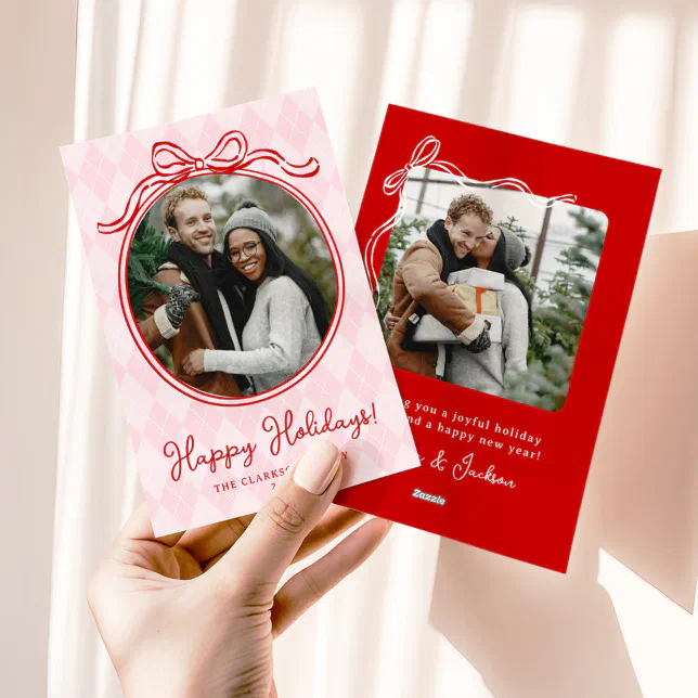 A hand is seen holding pink and red bow holiday cards.