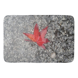 Red fall leaf in rain on grey textured road bath mat