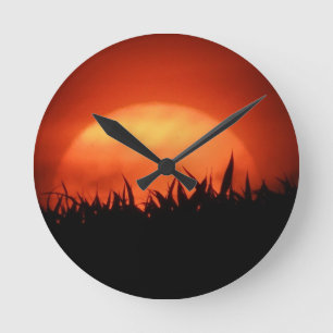Red sundown behind black grass round clock