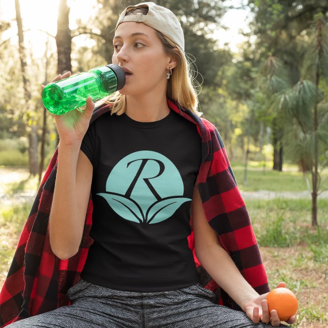 Rejuvenescents Icon- Body Care Brand T-Shirt (Young woman wears a black shirt with the Rejuvenescents "R" leaf logo. She sips water, holds orange.)