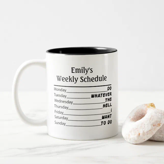 A white and black mug sits next to some donuts.
