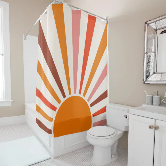 Large orange, pink, red and brown sun shower curtain shown in use in a bathroom. In the background there is a mirror, a white sink and a white toilet.