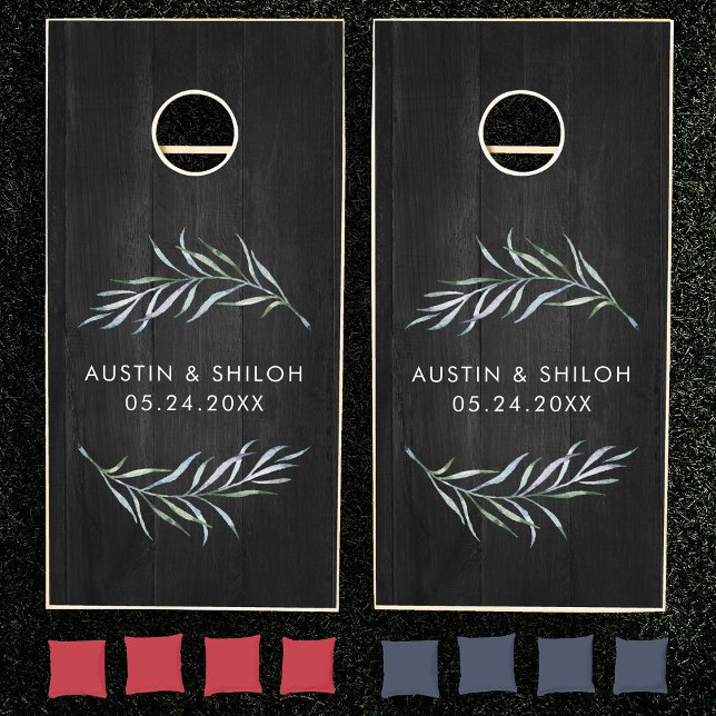 Romantic Botanical Greenery Elegant Black Wedding Cornhole Set (Two black cornhole boards on grass, each featuring a leafy branch design and personalized text)