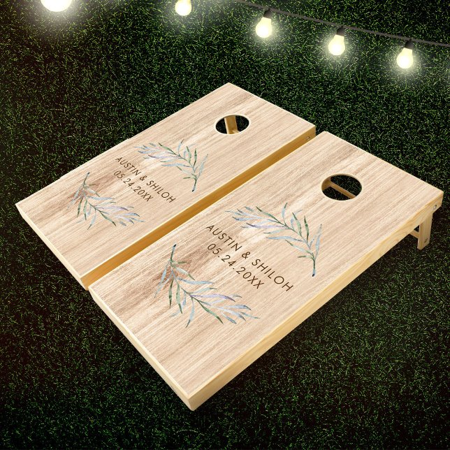 Romantic Botanical Greenery Modern Pine Wedding Cornhole Set (A cornhole set with floral accents and personalized text, "Austin & Shiloh 05.24.20XX," on grass)