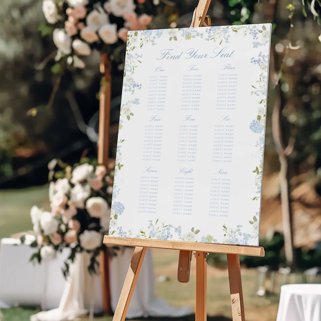 A dainty blue seating chart is standing on a light-wooden easel. There's pink and white roses in the background.