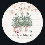 Rustic Christmas Trees Wood String Lights Classic Round Sticker<br><div class="desc">A rustic Christmas sticker featuring watercolor Christmas pine trees fresh from the tree farm,  string lights on a wood background,  with falling snow. Your family name on a light wood background. Pretty script type Merry Christmas. You may use the holiday text on the card or write your own.</div>