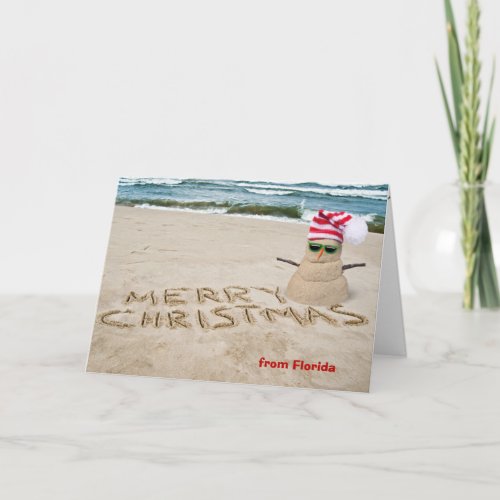 Sand snowman on beach with ocean holiday card