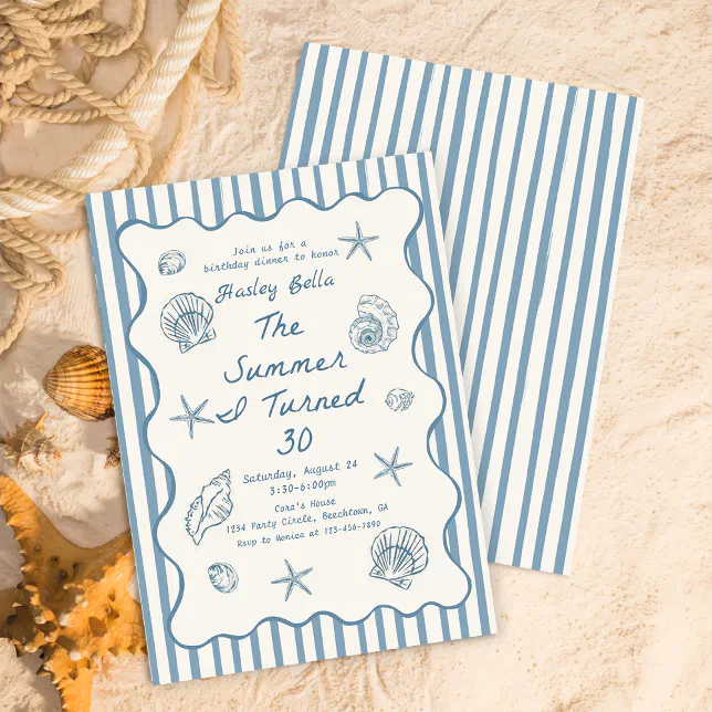 A blue and white striped invite is lying on a sandy surface. The invite has a seashell theme, and other seashells can be seen to the left of the invite.