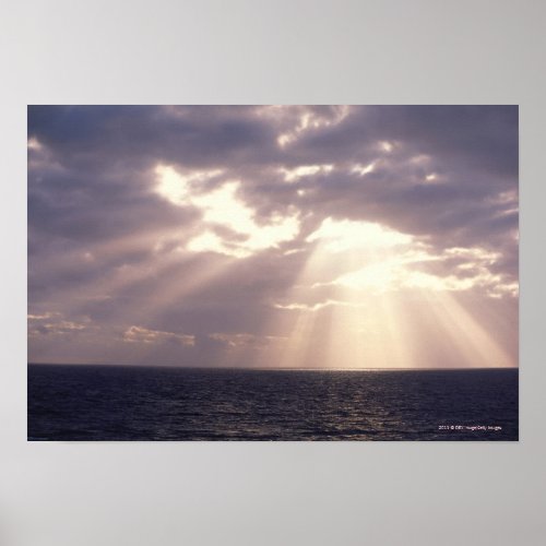 Setting sun shining through clouds over ocean poster