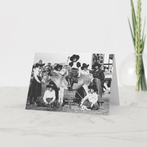 Seven rodeo cowgirls jokingly posing with a donkey card