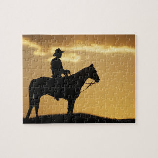 Silhouette of cowboy on horseback at sunset or jigsaw puzzle