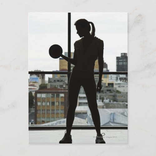 Silhouette of woman lifting weights at gym postcard
