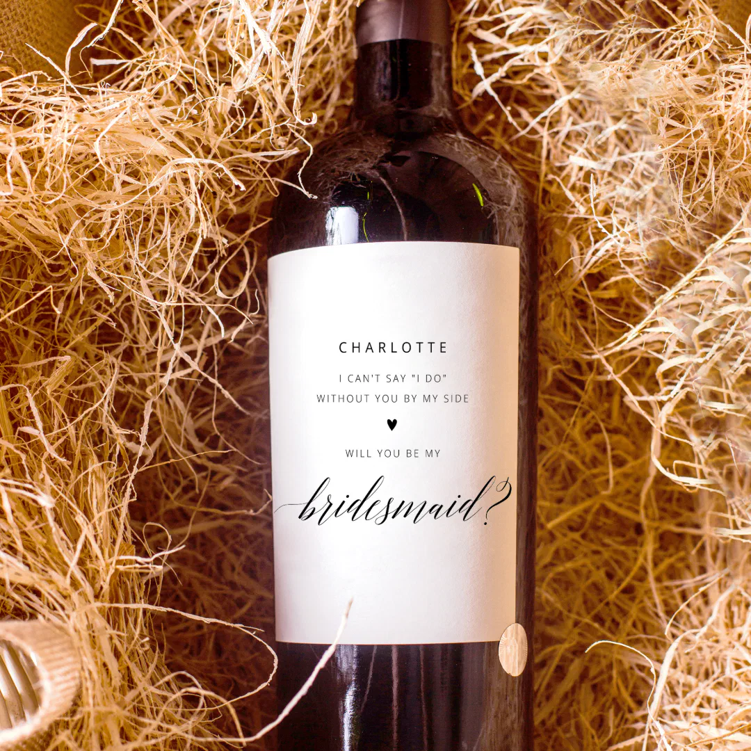 A bottle of red wine with a personalized white label displaying back text. There's also a little black heart separating the sentences. The wine bottle is resting in a pile of straw for the photo.