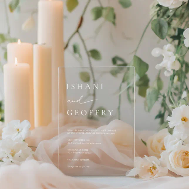 An acrylic wedding invitation standing in the middle of a display with candles and flowers. 