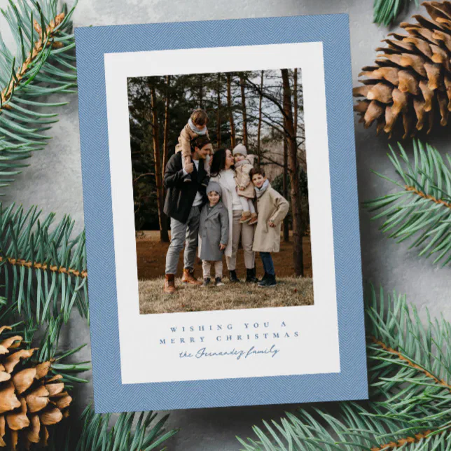 A blue framed holiday card surrounded by fir tree leaves and pine cones.